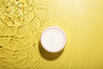 Jar with cream in water on yellow background, top view. Cosmetic product