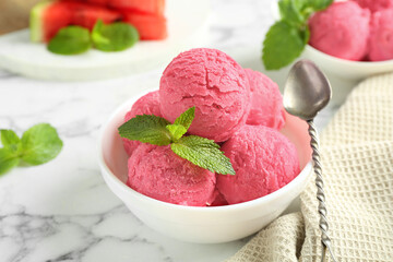 Scoops of tasty watermelon sorbet with mint in bowl and spoon on white marble table, closeup