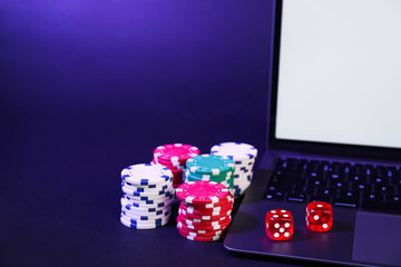 Online poker. Chips, dice and laptop on dark table, closeup
