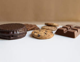 Alfajor argentino cubierto de chocolate, galletas con chips y barra de chocolate ante fondo de papel kraft.  