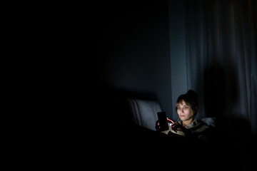 young woman staring at cell phone with face illuminated by screen late at night on sofa © nikopacheco
