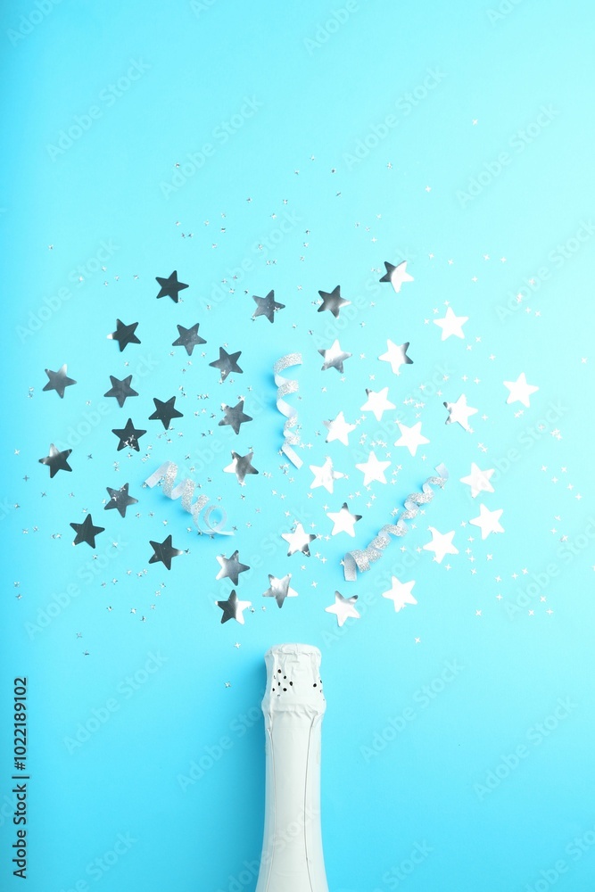 Wall mural Confetti and bottle of sparkling wine on light blue background, flat lay. Christmas decor