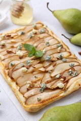 Delicious puff pastry tart with pears, almond, mint and blue cheese on light table, closeup