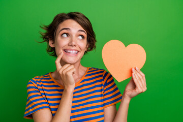 Portrait of gorgeous minded person finger touch chin hold heart card look empty space isolated on green color background