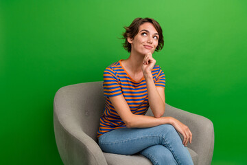 Portrait of cute creative person sit comfy chair arm touch chin look empty space isolated on green...