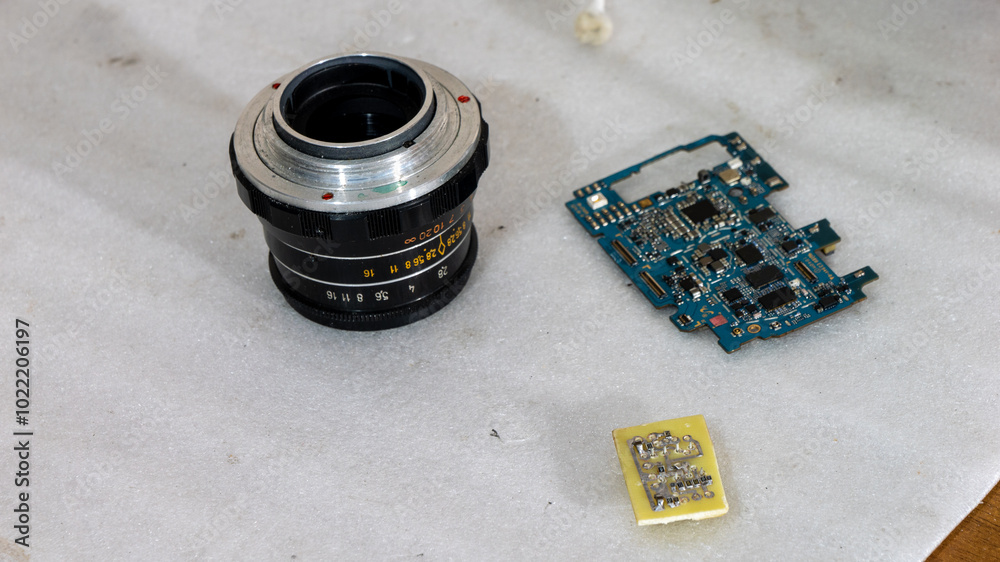 Poster a camera lens and a circuit board are laying on a white surface