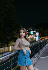 Beautiful brunette asian woman standing relaxed and leaning on outdoor balcony at night. Leisure and people concept.