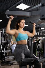 Fototapeta premium Young female training trains the muscles of the arms and press on the simulator in gym. Sport concept