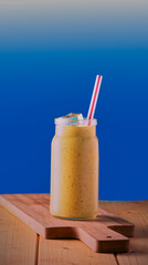 Healthy smoothie in a jar with a straw and ice on a blue gradient background.