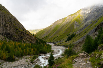 A scenic view of a winding river surrounded by lush green mountains in a remote valley during cloudy weather