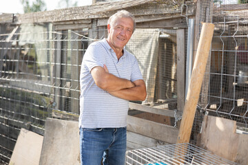 Portrait of an elderly farm owner with a chicken coop in the background © JackF