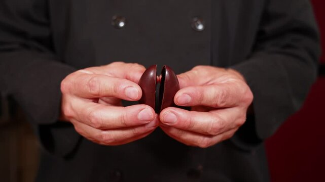 Chocolatier in a black chef's jacket opens and closes a chocolate easter egg, showcasing skill and craftsmanship. Selective focus