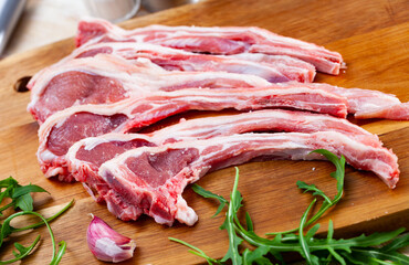 Fresh raw young mutton chops on wooden cutting board with herbs and spices prepared for cooking on kitchen table. Healthy organic food