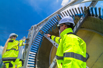 Two engineers in safety gear inspecting a wind turbine blade section on a construction site. They examine the metal framework with precision. Renewable energy project under a clear blue sky.