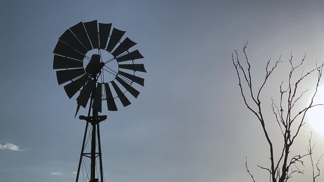 Silhouette of wind pump pumping water in a farm in the outback of Queensland, Australia. 