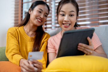 Two Young Women Shopping Online Together Using a Tablet and Credit Card in a Cozy Living Room Setting