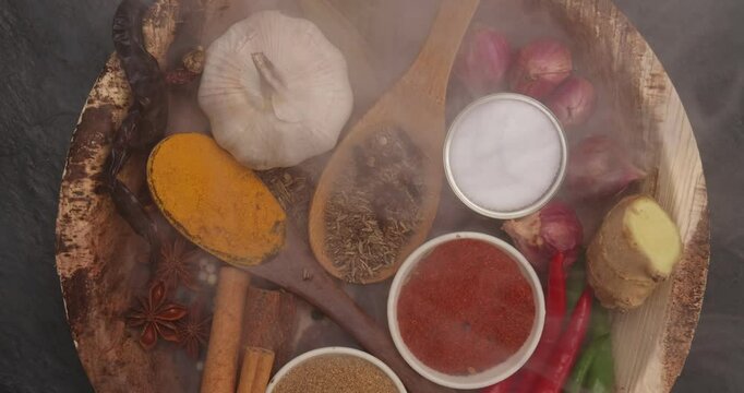 Asian favour spice green red dry chilli powder onion garlic ginger cinnamon cardamon turmeric fennel seeds bay leaf clove star anise wooden spoon blows on palm leaf plate over black slate background