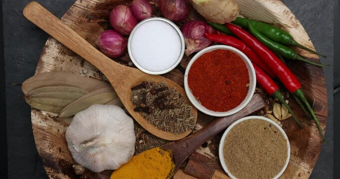 Asian favour spice green red dry chilli powder onion garlic ginger cinnamon cardamon turmeric fennel seeds bay leaf clove star anise wooden spoon blows on palm leaf plate over black slate background