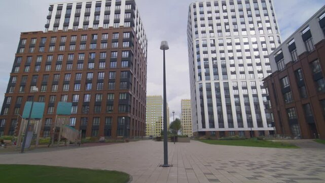 Flower beds with greenery stand in paved walkway area FPV. City center features office buildings standing in pedestrian rest area with playground