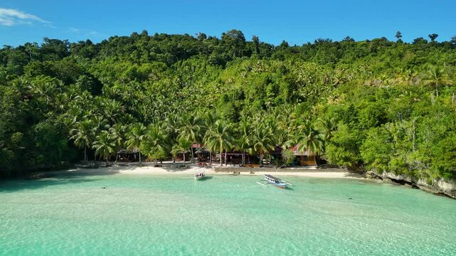 INDONESIA - 9.4.2024 - Great aerial footage pulling back from tourists swimming and boating off the shore of Indonesia's tree-covered Malenge Island.