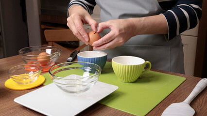 Process of making dough. Woman separates egg white from yolk in kitchen. Scales and eggs, utensils on wooden table. Baking macarons at home. Hands in close-up.