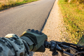 Cyclist's hand in a glove on the handlebars, leaving the side of the road on an asphalt road