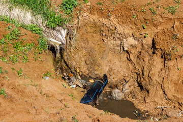 A stream of water flowing down a gutter washes away clay soil