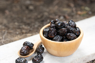 Close-up of a wooden bowl filled with dried date palm, accompanied by a wooden spoon holding a few dried date palm on a rustic white surface.