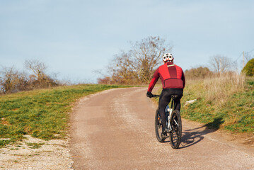 Naklejka premium Cycliste sur une route de campagne. Montée à vélo. Faire de la bicyclette en hiver. Balade en campagne. Promenade rurale. Seul à vélo. Protection en vélo