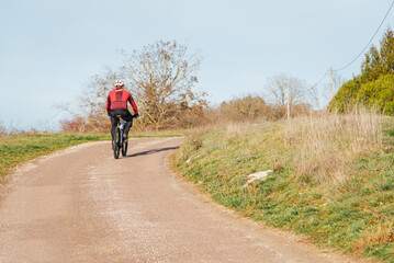Obraz premium Cycliste sur une route de campagne. Montée à vélo. Faire de la bicyclette en hiver. Balade en campagne. Promenade rurale. Seul à vélo. Protection en vélo