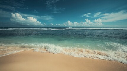 A pristine beach with soft white sand and turquoise water lapping at the shore under a bright blue sky.