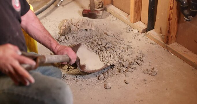 Construction worker scraping broken concrete with a shovel in slow motion, showcasing manual labor and renovation efforts. Selective focus