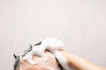 Male hands wash their hair with shampoo and foam on gray tile background, front view.