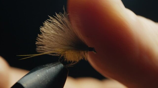 Person trips handmade fishing fly locked in the vice on the solid studio background. Macro studio footage of the fishing fly