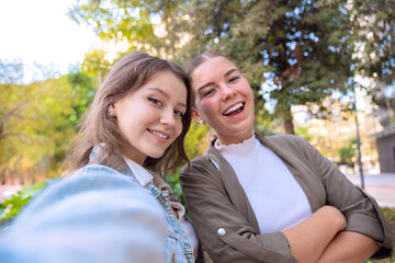 Happy female friends taking a self portrait with cell phone and smiling outdoors