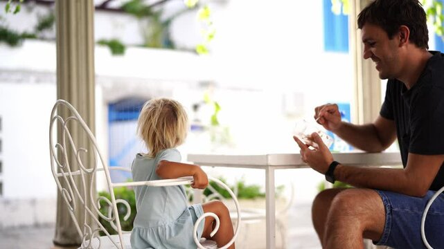 Dad feeds a little girl with porridge from a spoon while sitting on chairs in the garden. High quality 4k footage