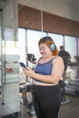 Obese asian woman Enjoy listening to music. Fat Female with headphones smart phone after workout at Gym