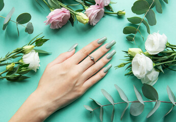 Elegant hand with manicured nails surrounded by fresh flowers and greenery on a turquoise background