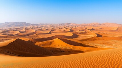 A vast expanse of red sand dunes stretches out under a clear blue sky.