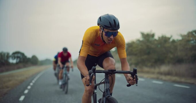 Lead Cyclist Pedals Ahead with Two Riders Following in Slipstream Close Behind. Professional Team Training on a Cloudy Day, Each Athlete Focused on Pushing Themselves Further During the Ride