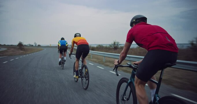 Professional Cycling Team Racing on a Seaside Road, Showcasing Endurance and Teamwork. Cyclists, Wearing Colorful Jerseys, Drafting Together, Practicing for a Cycling Competition. Back View Footage