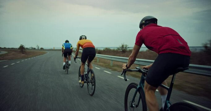 Cycling Team Pedal Together on a Windy Coastal Road, Cyclists Train Before a Big Competition. Professional Athletes Dedicated to the Sport, Pushing Forward on a Cloudy Day. Back View Footage