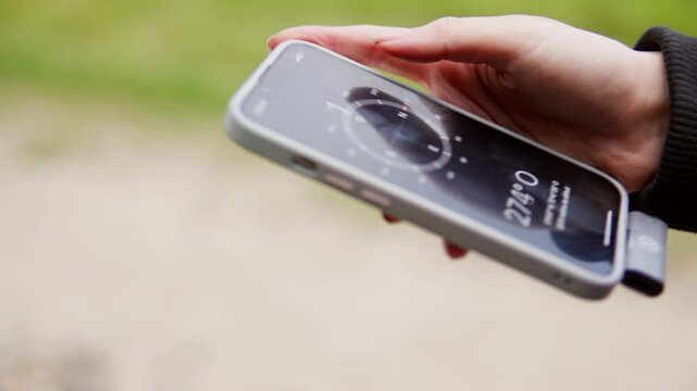 Hand holding a smartphone displaying a compass app with green nature background