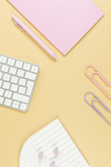 Top view of white keyboard, pink notebook, pink pen on yellow background. Paper clips, pins, modern office, school. White arch tray, flat lay, copy space.