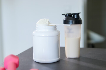 Close up of a protein shake in a bottle on table with pink dumbbells and white whey protein powder in a scoop. Diet meal replacement for weight loss. 