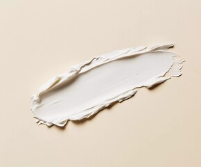 Photograph of a single smudge or swatch of white cream isolated on a beige background,