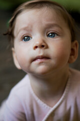 A baby or infant or a small child or a girl looks up with big blue eyes, frowns discontentedly and drools. Portrait of a child close-up