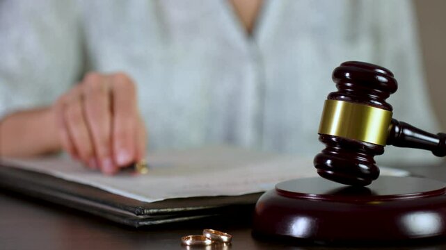 Signing divorce document. Wedding rings and gavel with a woman signing a contract, close-up, selective focus