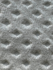 This image displays a close-up of a light gray, soft-textured material with small diamond-shaped indents, giving it a quilted or padded appearance.