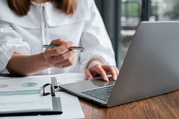 A business professional working on a laptop and analyzing financial charts and graphs on documents at an office desk.